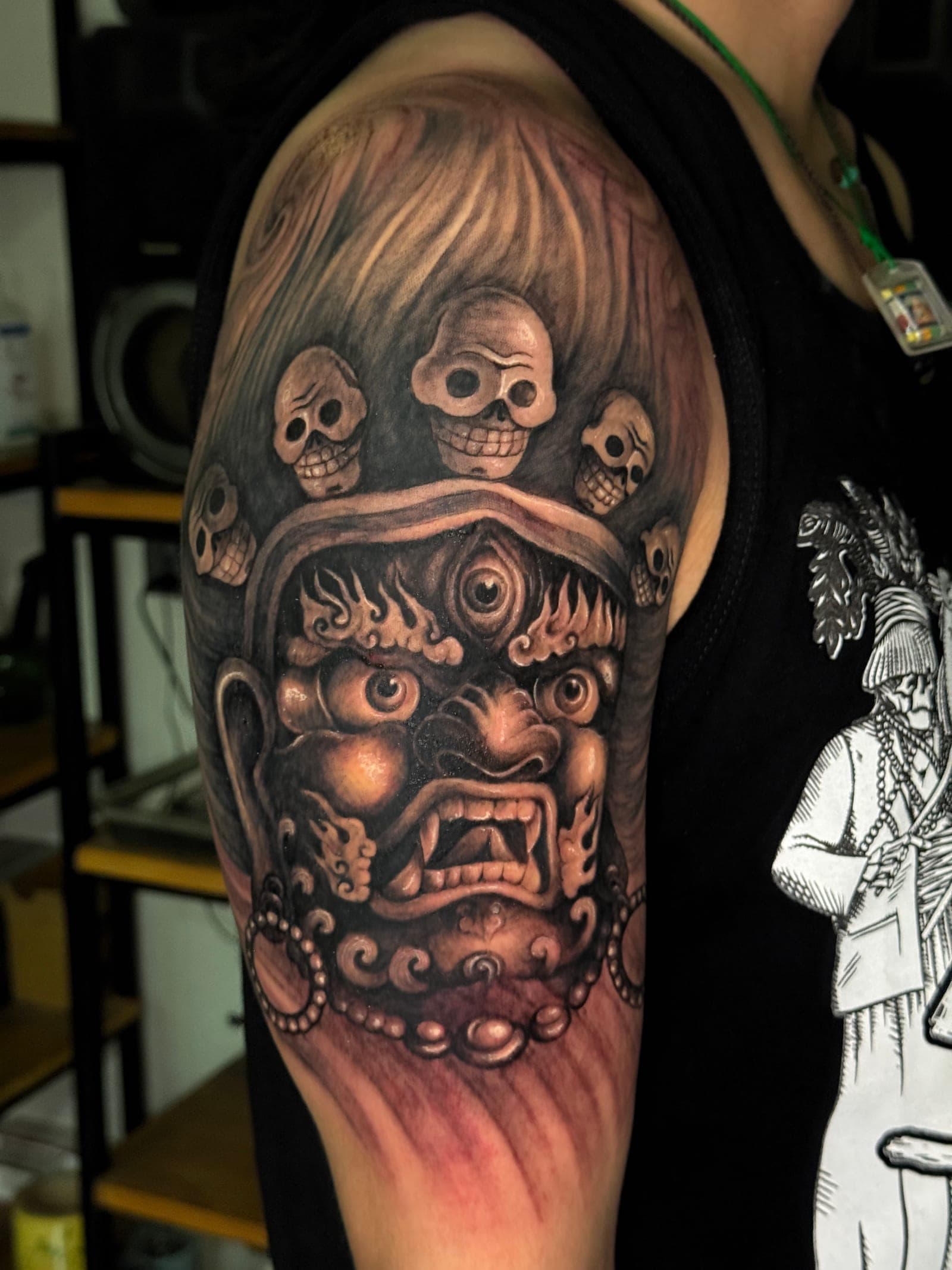 Mahakala shoulder tattoo with skull crown and flame motifs in black and grey